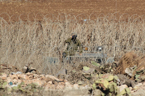 At the edge of the West Bank village of Faqqua, an Israeli soldier watches from the other side of the Green Line. Photo by Bryan MacCormack of Left in Focus.